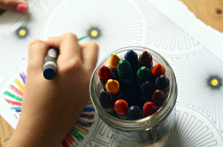 child coloring with a crayon and a jar of crayons next to hand