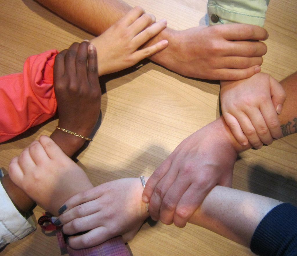 seven people holding each others' wrists in a circle over a wooden table - homeschooling resources
