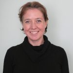 Smiling woman facing camera against a grey wall